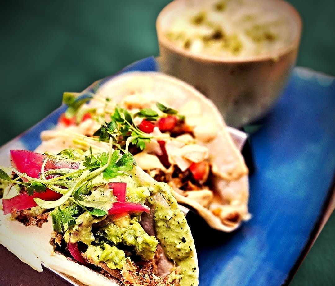 two carnitas street tacos with a cup of coleslaw